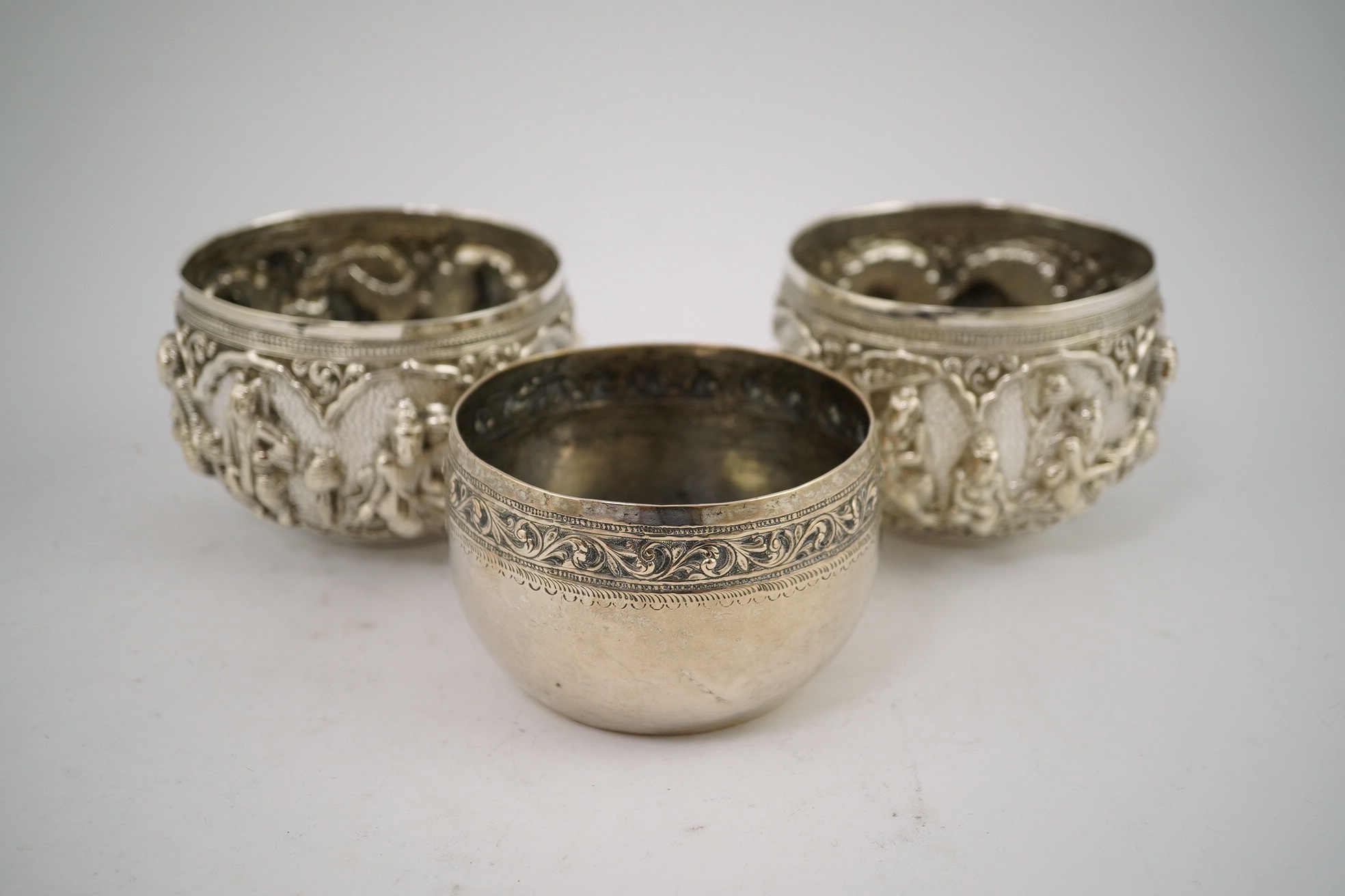 A pair of Burmese white metal bowls, embossed with figures, 12cm diameter, 220 and 224g and a plainer bowl, 110g. Condition – fair